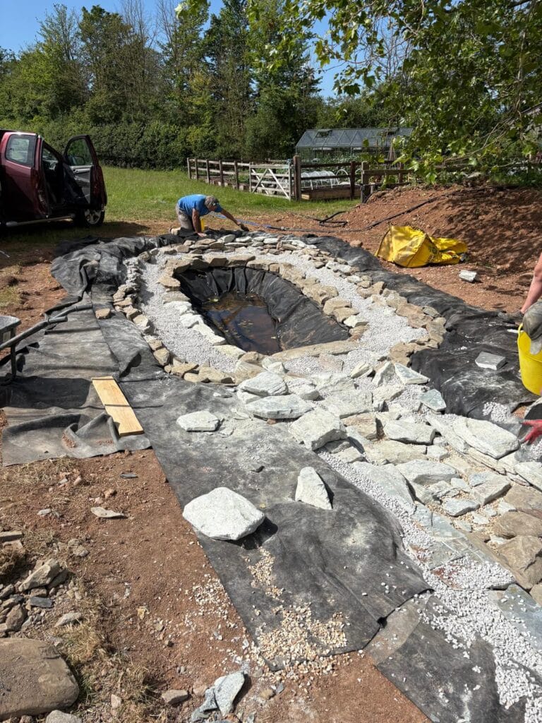 Liner and stone edging being installed along a wildlife pond channel